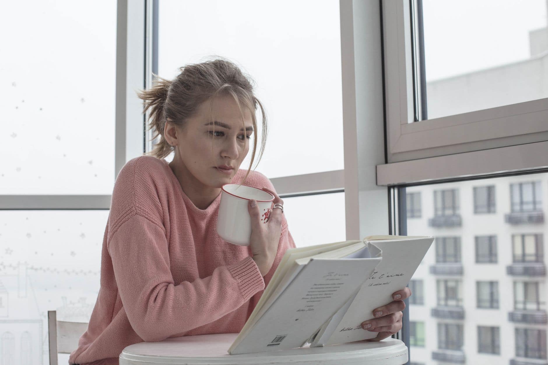 Casual woman enjoying a book with coffee by a bright window scene.