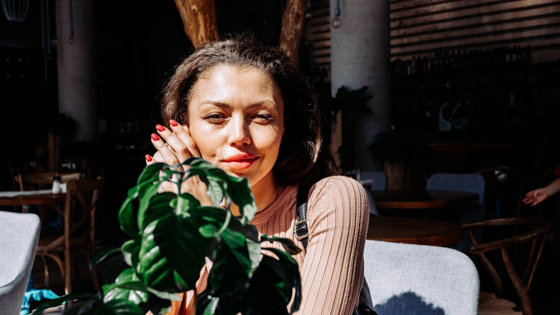 Una mujer adulta sonríe junto a una planta en el interior de un café.