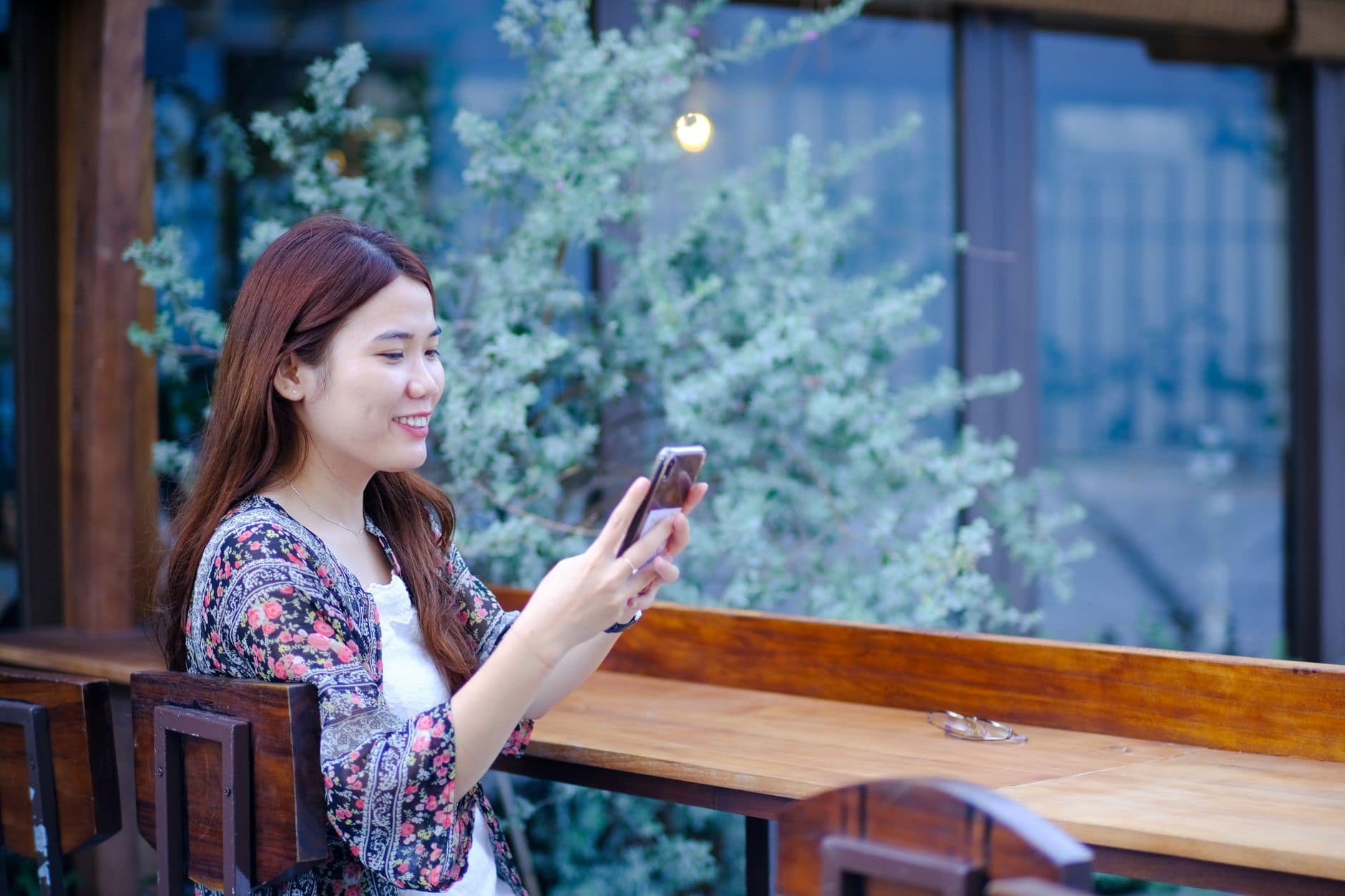 Una mujer adulta sonríe mientras mira el celular junto a una mesa de madera.
