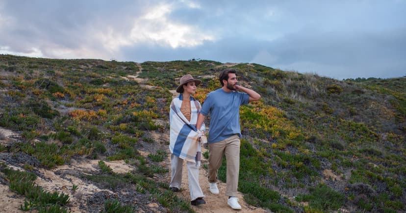 A couple walking together down a sandy path through green coastal hills under a moody evening sky