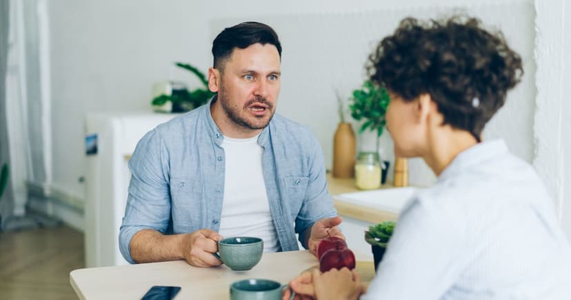 A man and a woman having a serious conversation over coffee at a kitchen table