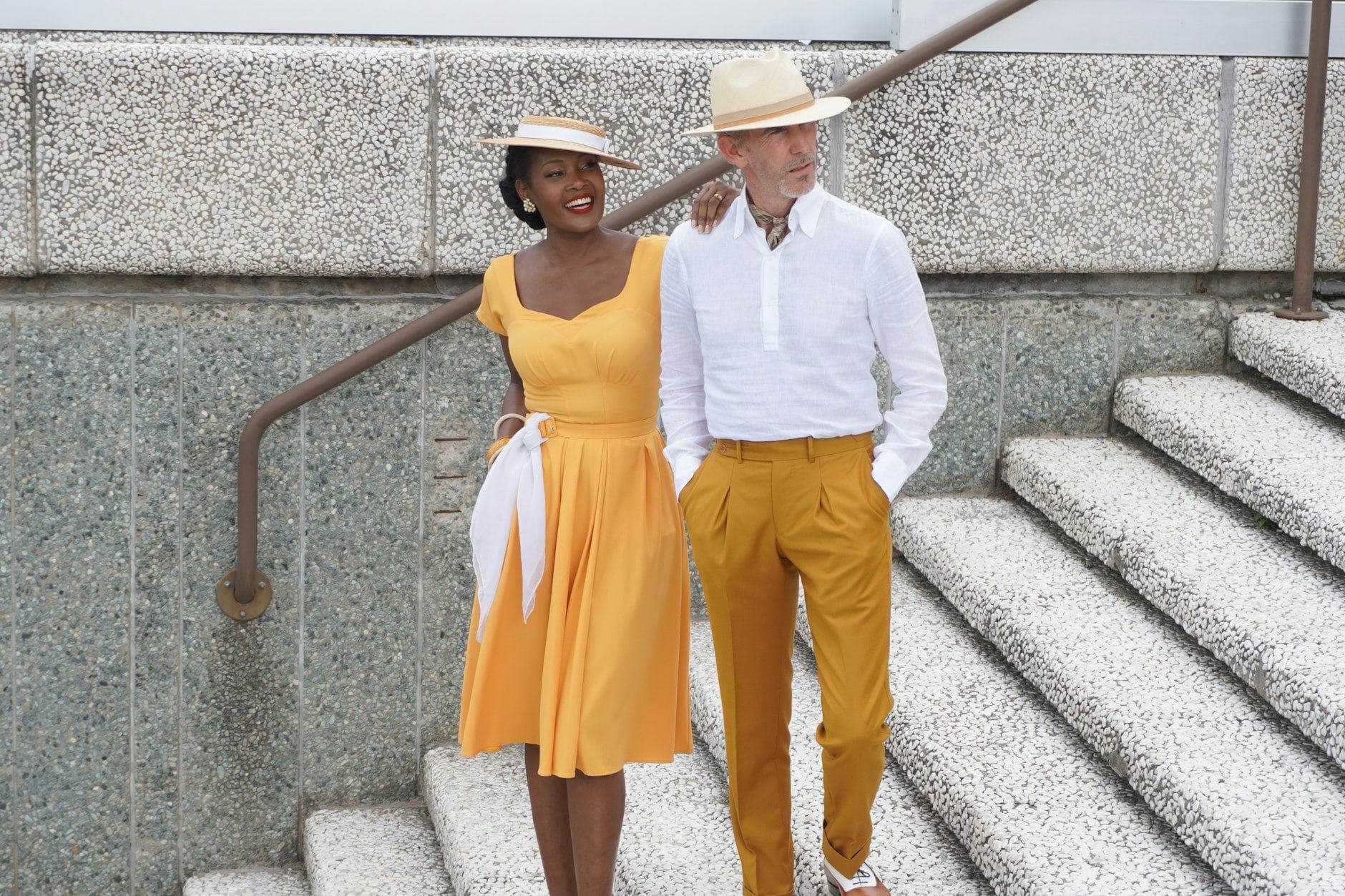 Una coppia elegante scende una scalinata in pietra a Firenze, lei in abito giallo e lui in lino bianco.