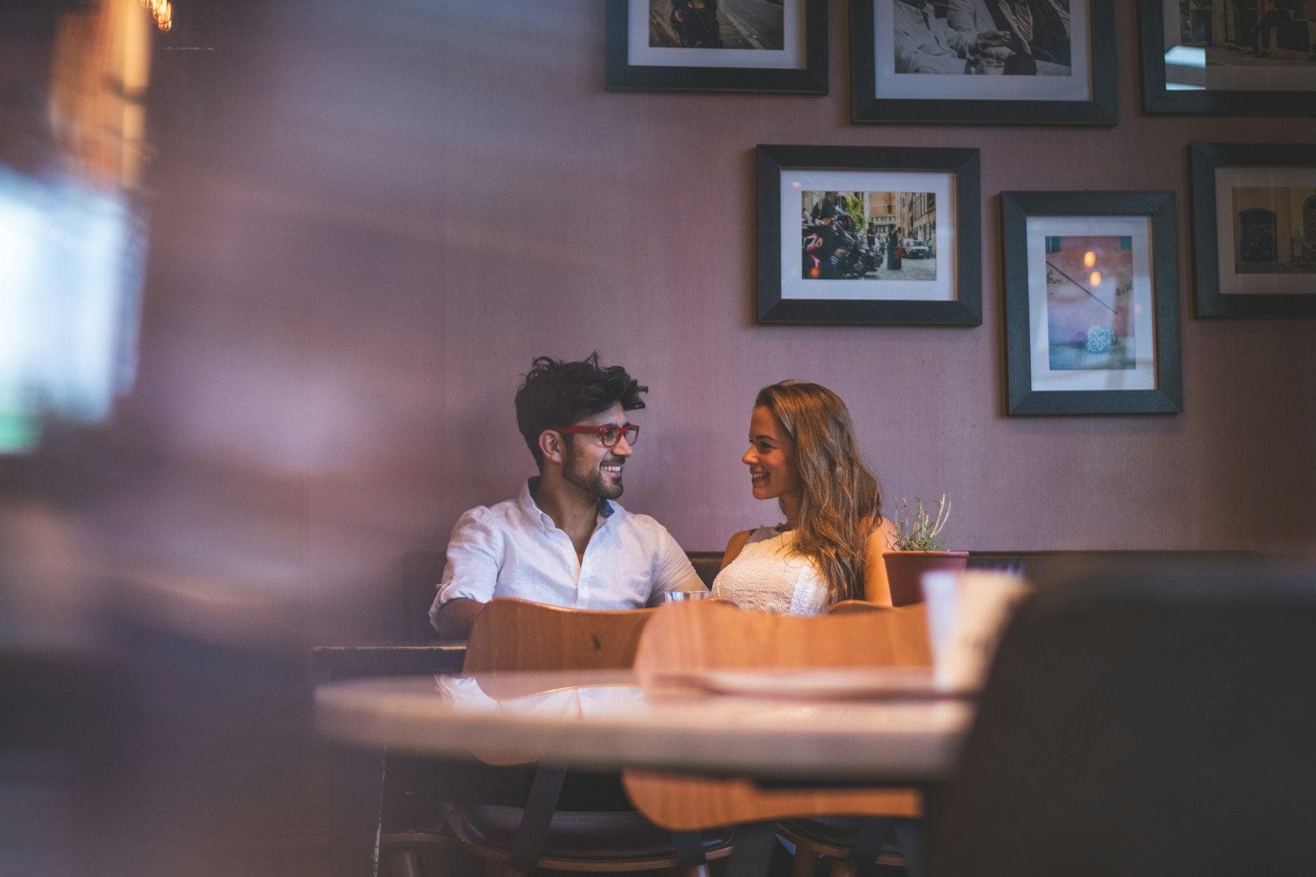 Un homme en chemise blanche et une femme discutent à table dans un restaurant à la lumière chaleureuse.