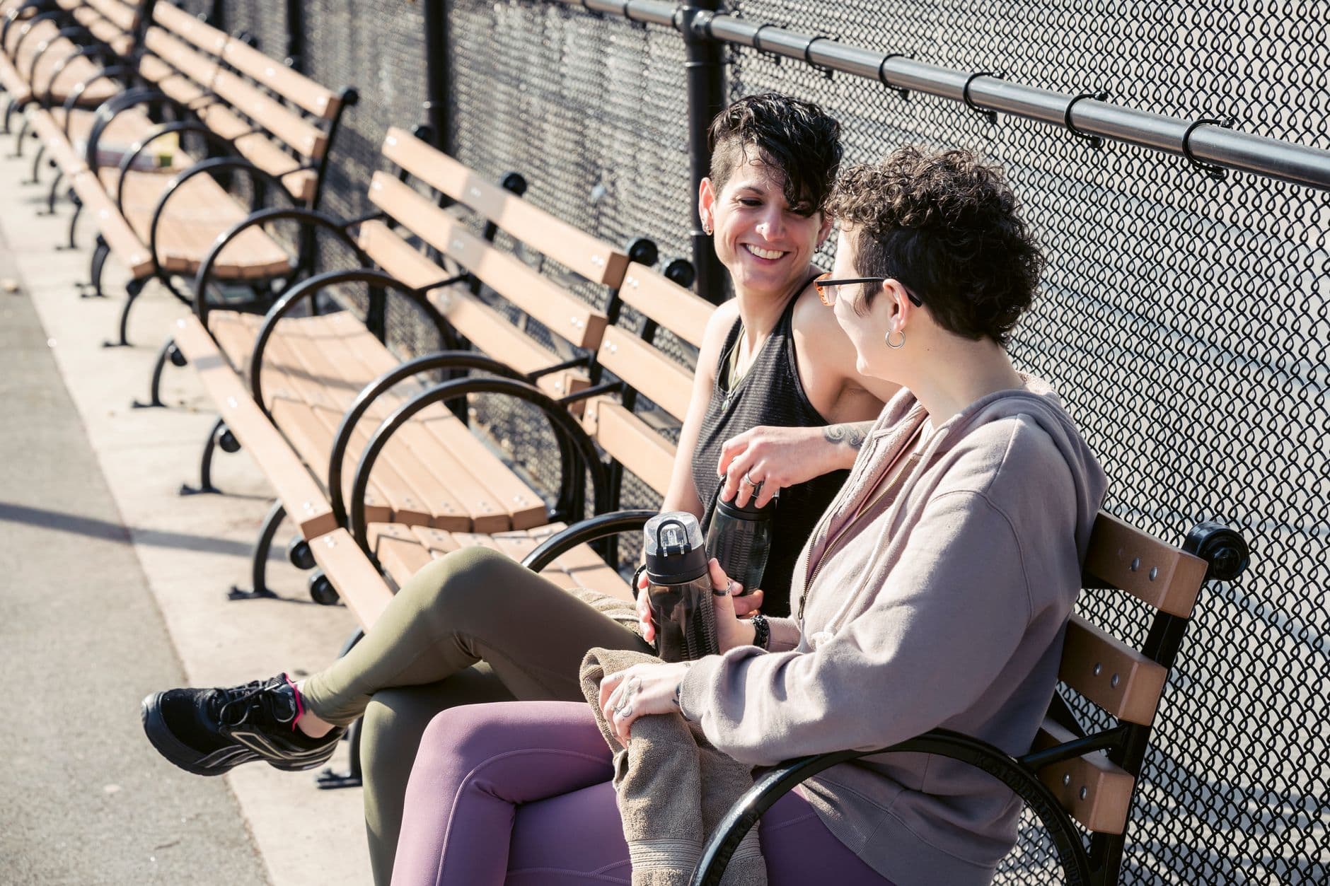 Deux personnes discutent en souriant sur un banc de parc, au soleil.