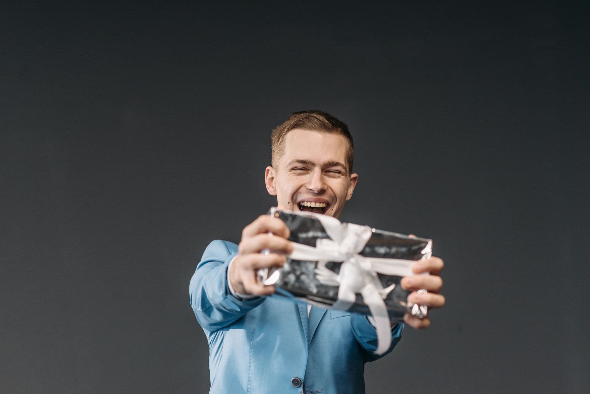 Un homme souriant en veste bleue tend un cadeau emballé vers l'objectif.
