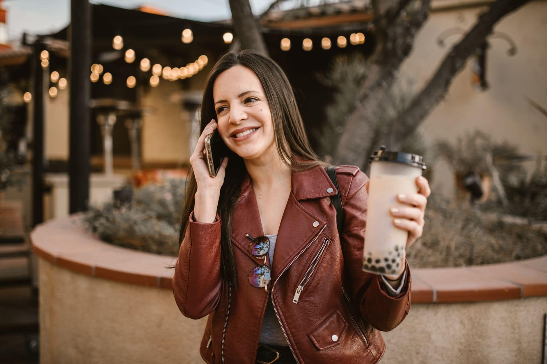 Una mujer adulta habla por celular mientras sostiene una bebida frente a un café.