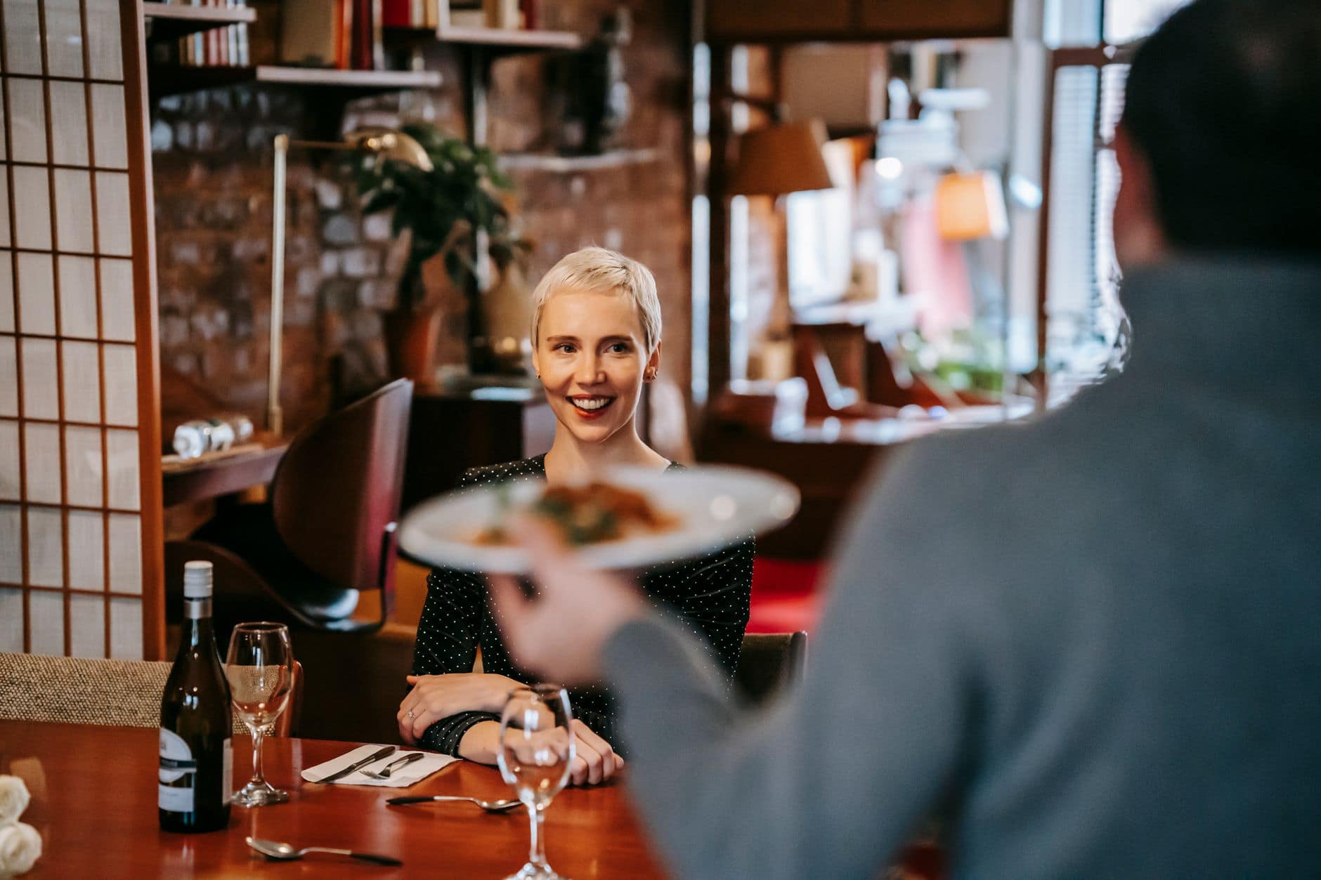 Una donna sorride al tavolo di un ristorante mentre un uomo le porge un piatto.