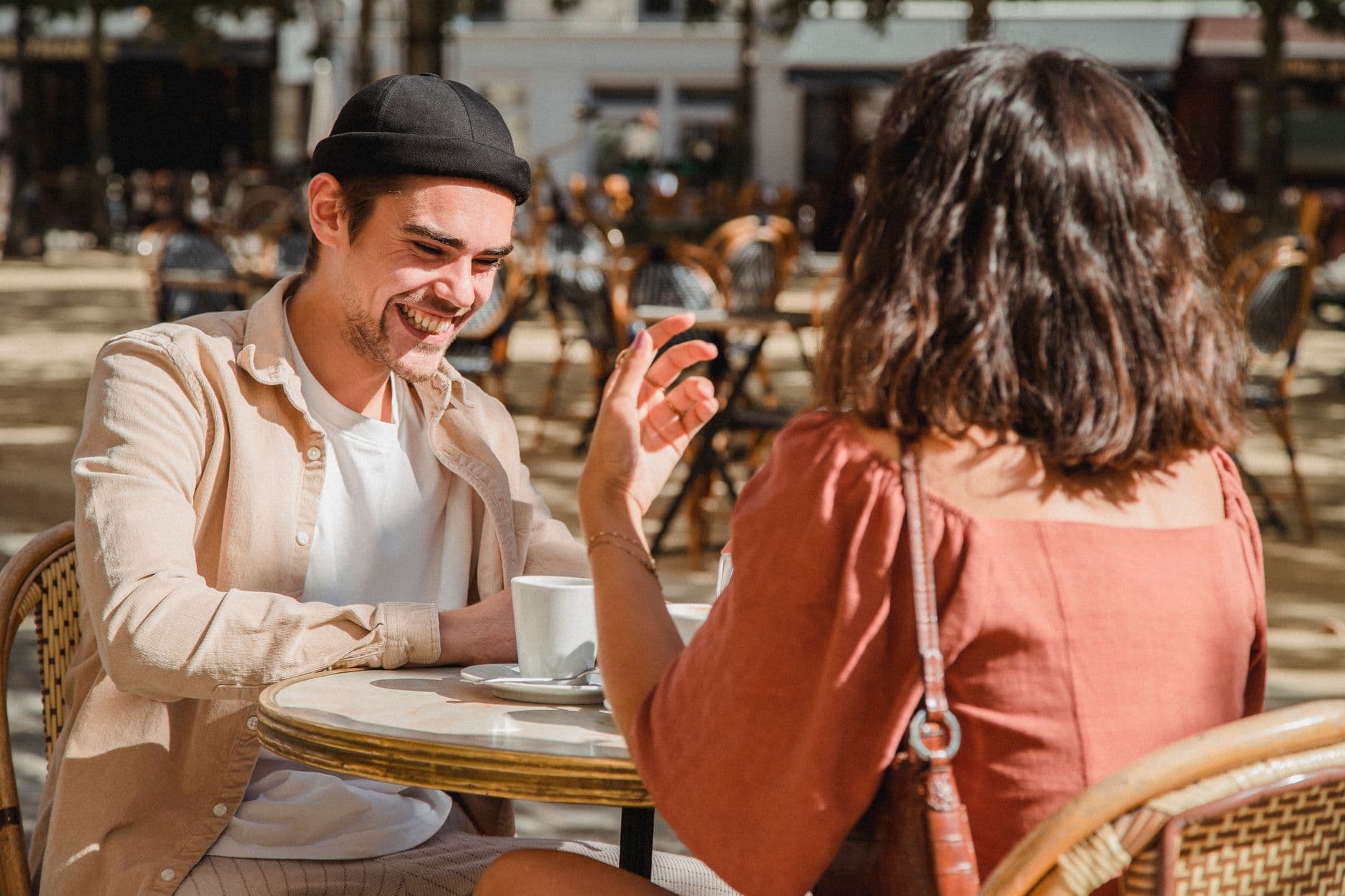 Un uomo sorride mentre conversa con una donna a un tavolino all'aperto.