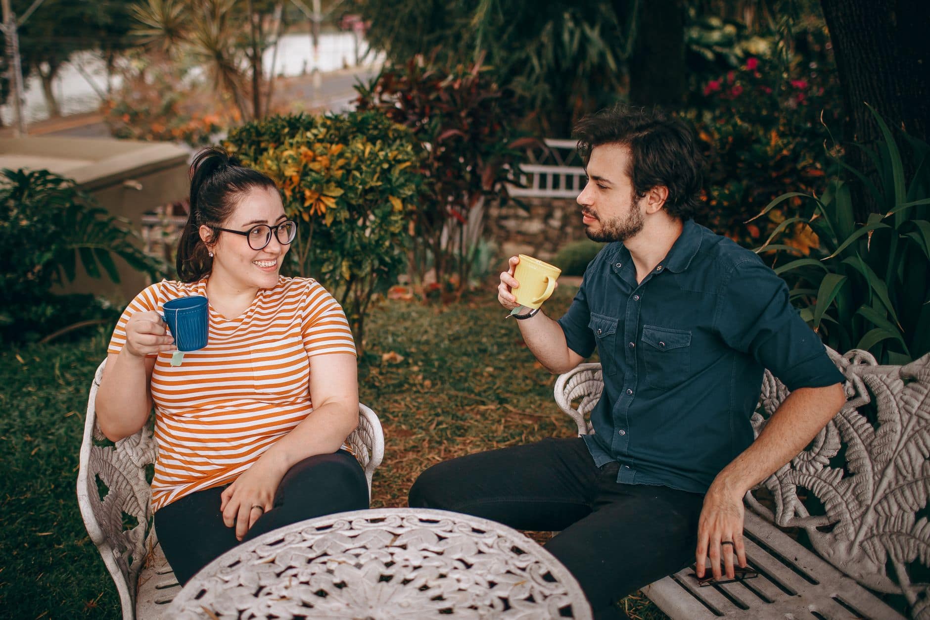 Ein Paar unterhält sich im Garten eines Cafés und hält bunte Tassen in den Händen.