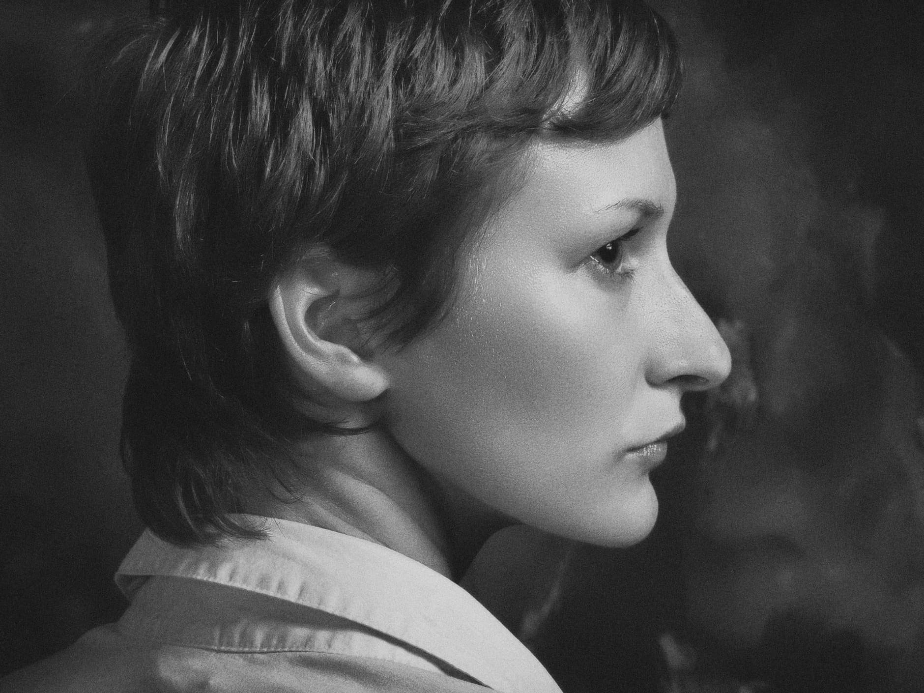 Monochromatic side-profile portrait of a woman with short hair taken indoors in a studio setting.