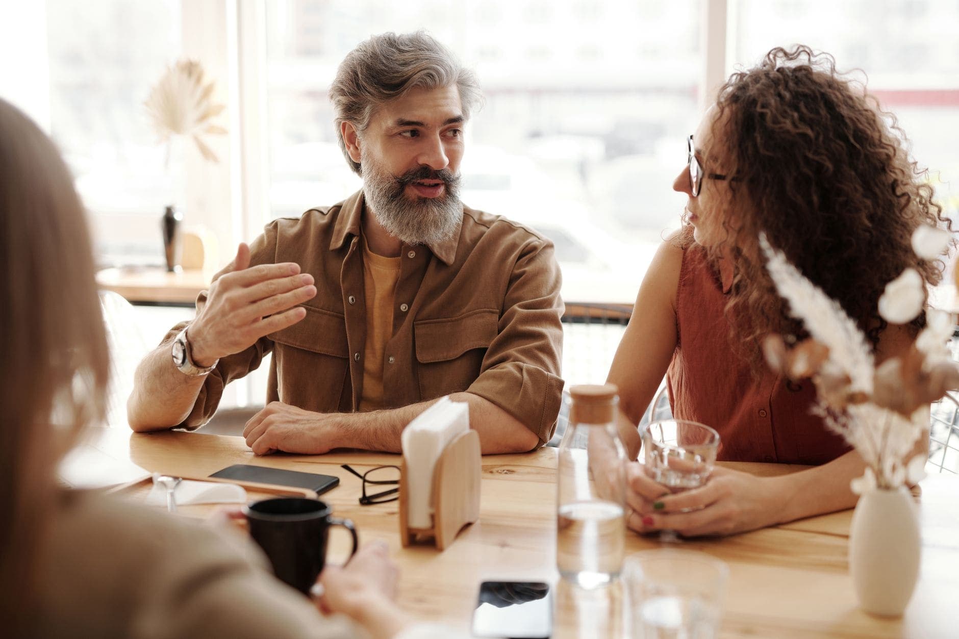 Um homem explica algo com um gesto de mão e uma mulher ouve atenta numa mesa de café