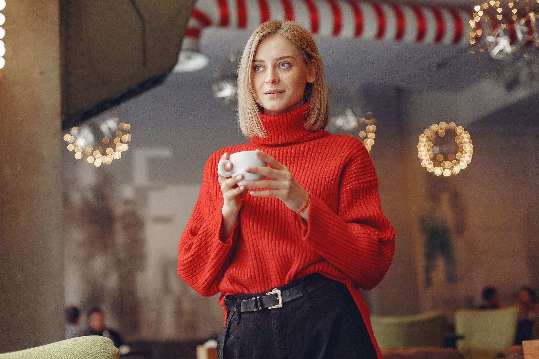 Uma mulher de camisola vermelha segura uma chávena branca e olha para o lado num café.