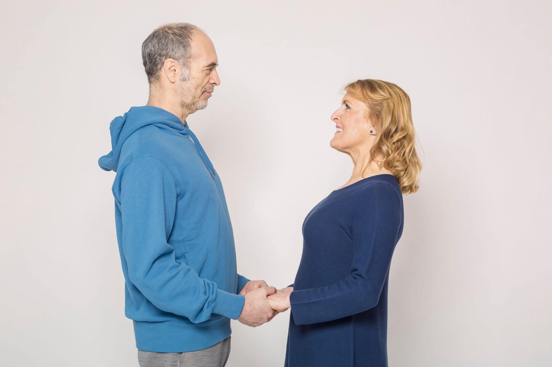 Dos personas adultas se toman de las manos y se miran frente a una pared clara.