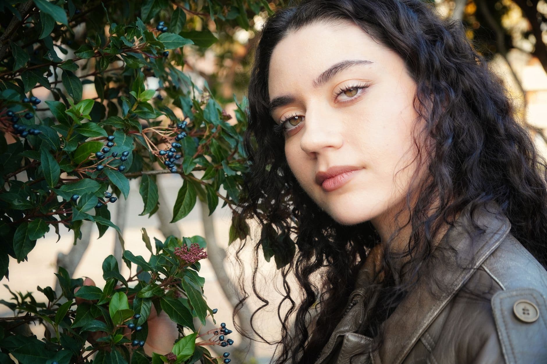 Ritratto di una donna dai capelli ricci accanto a una pianta verde.