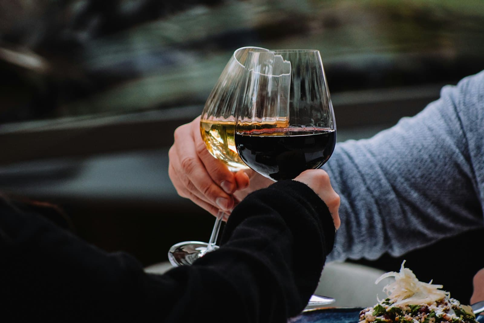 Zwei Hände stoßen beim Abendessen mit Weißwein und Rotwein an
