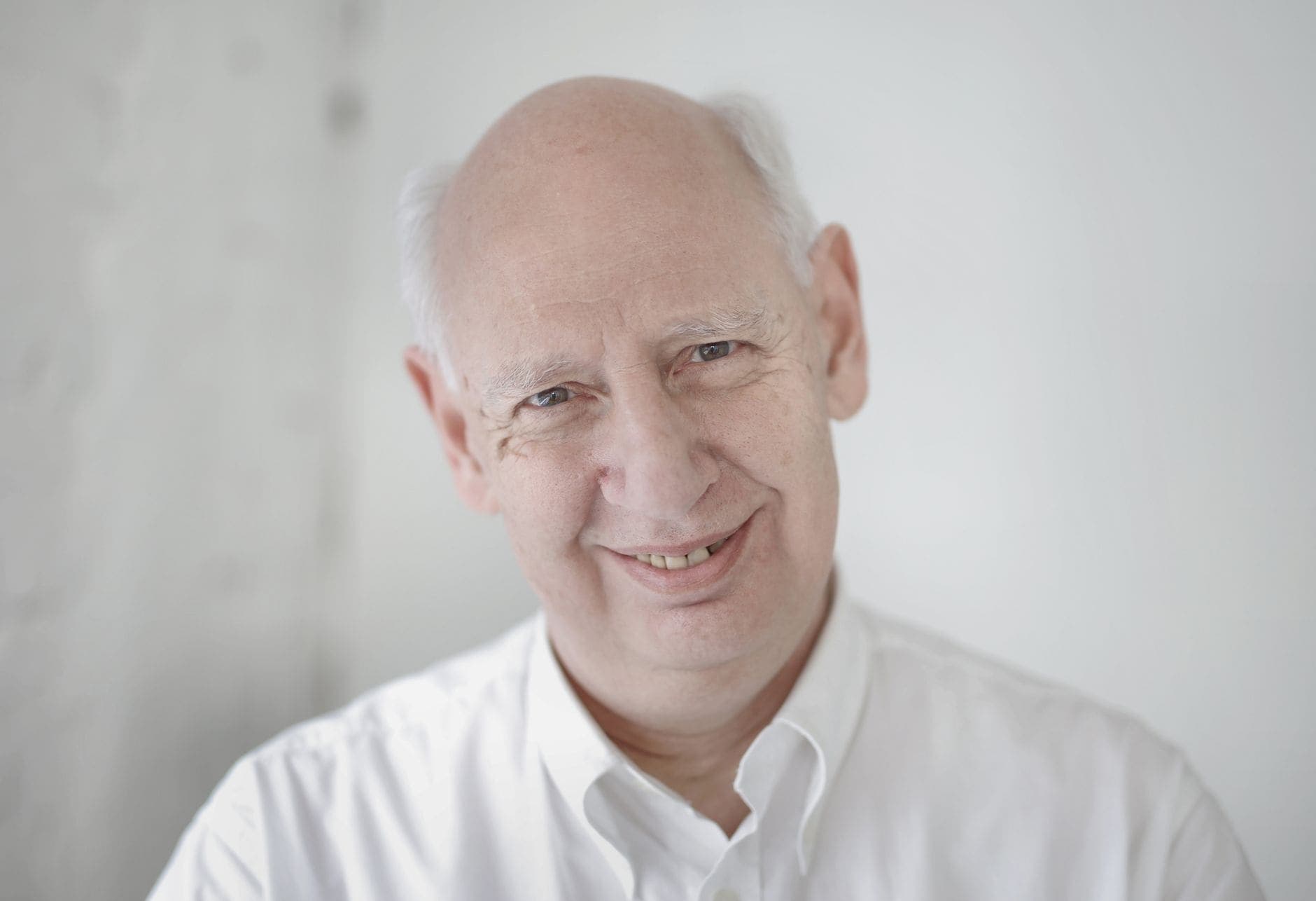 A man in a white shirt smiles towards the camera against a pale background.