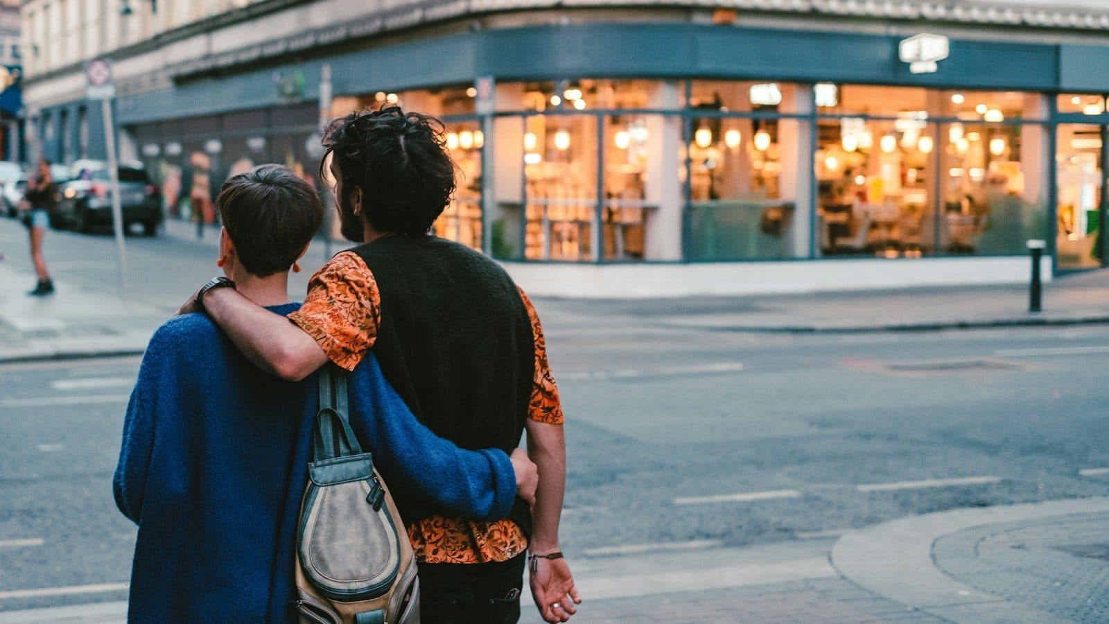 A couple seen from behind, arm in arm, at a Dublin street corner in the early evening