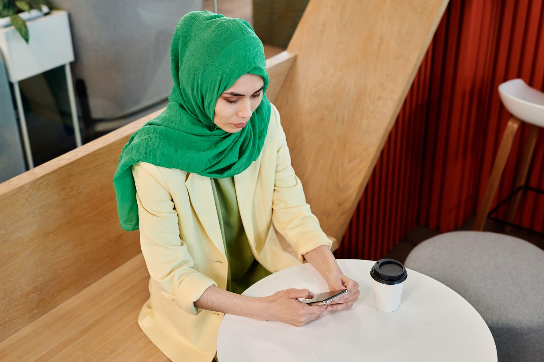 Una mujer adulta con un pañuelo verde mira su celular en una mesa de café.