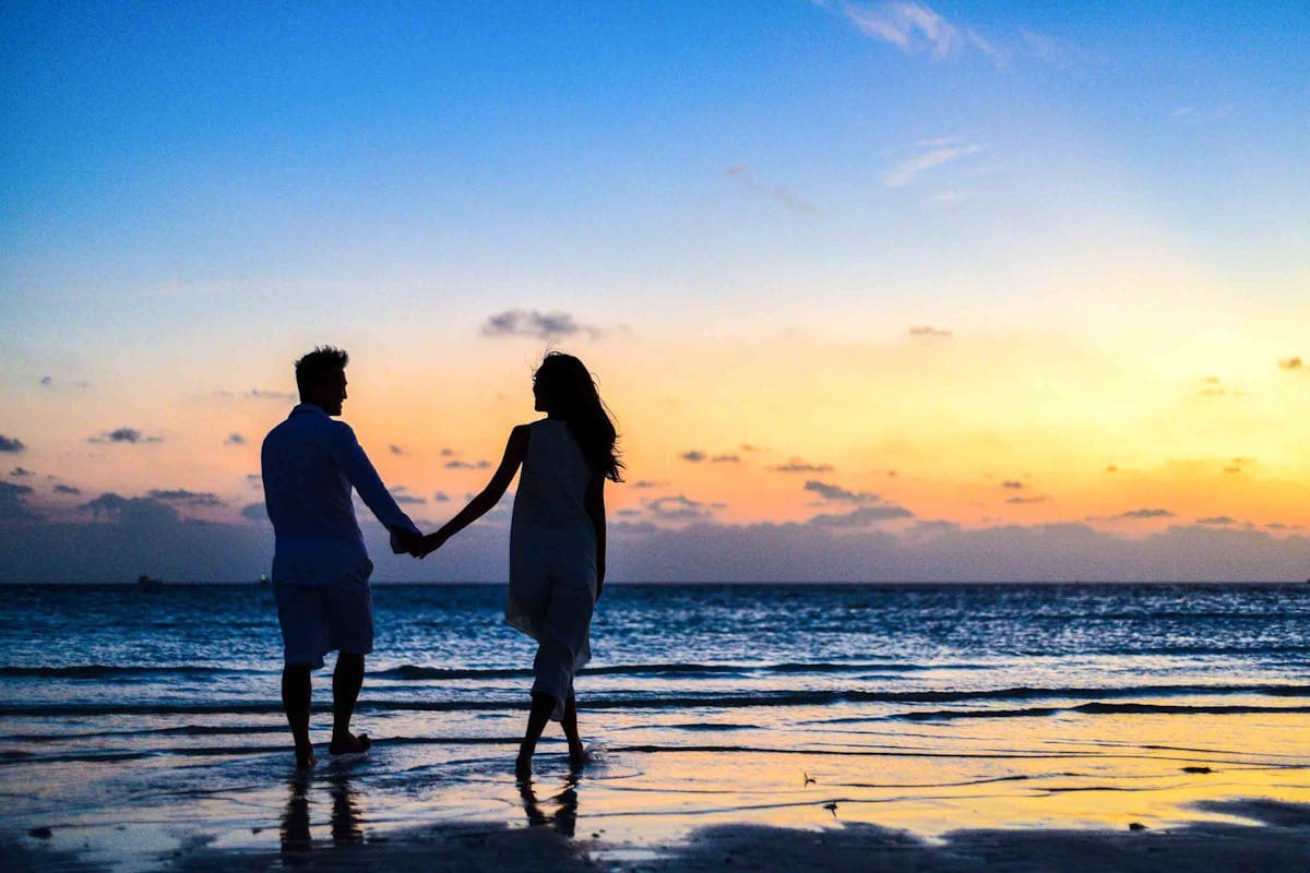 Twee mensen lopen hand in hand door het ondiepe water op het strand bij zonsondergang.