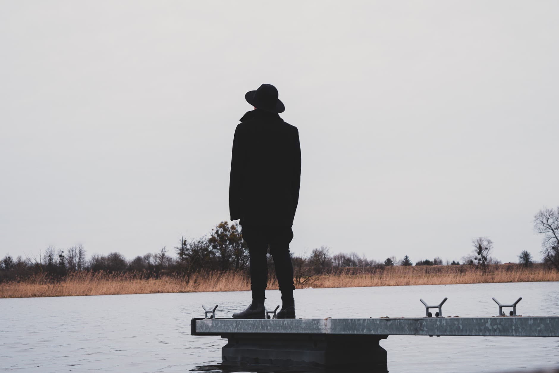 Eine Person steht als dunkle Silhouette auf einem Steg am See.