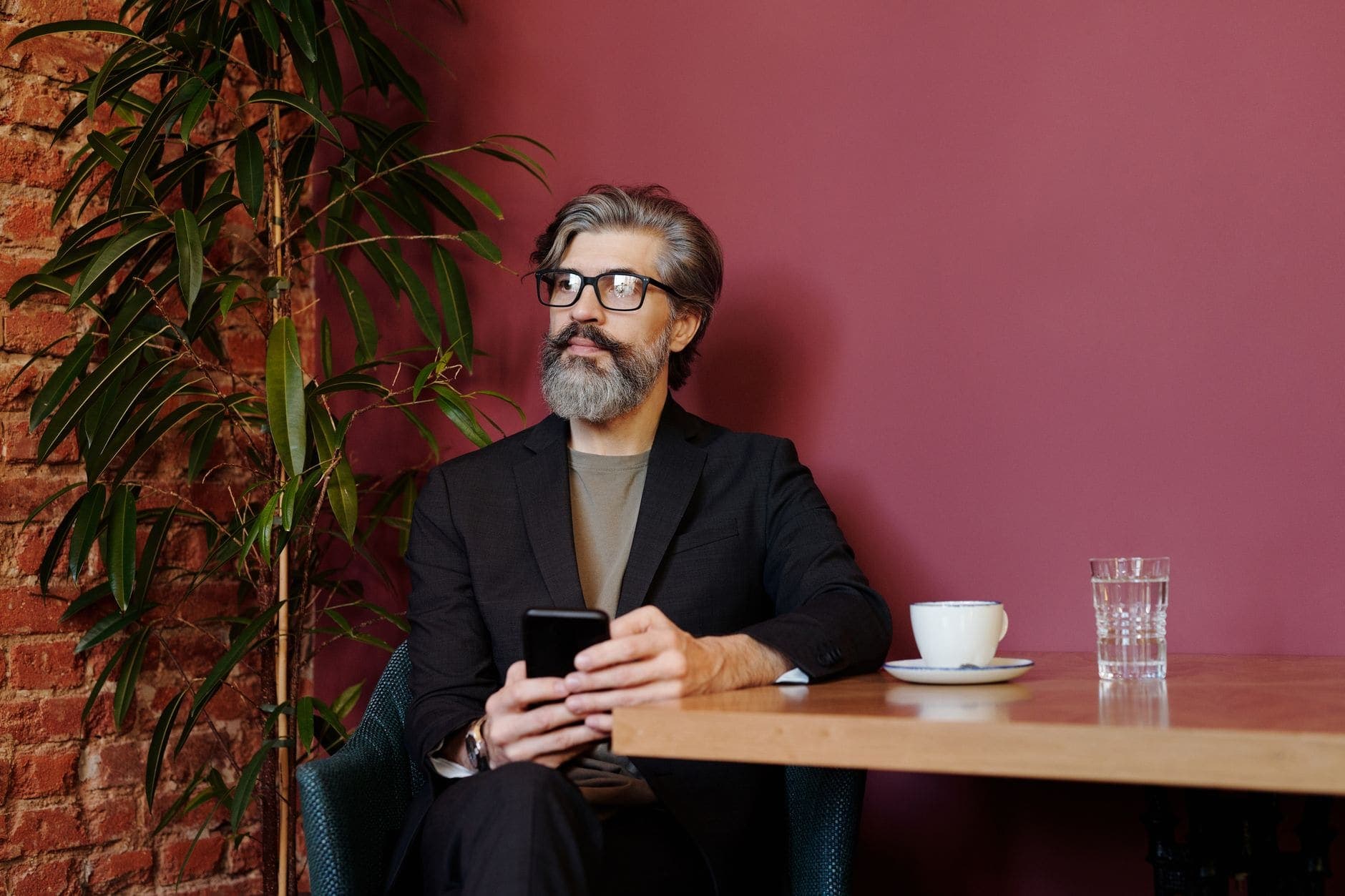 Um homem de barba grisalha segura um telemóvel à mesa e olha para o lado.