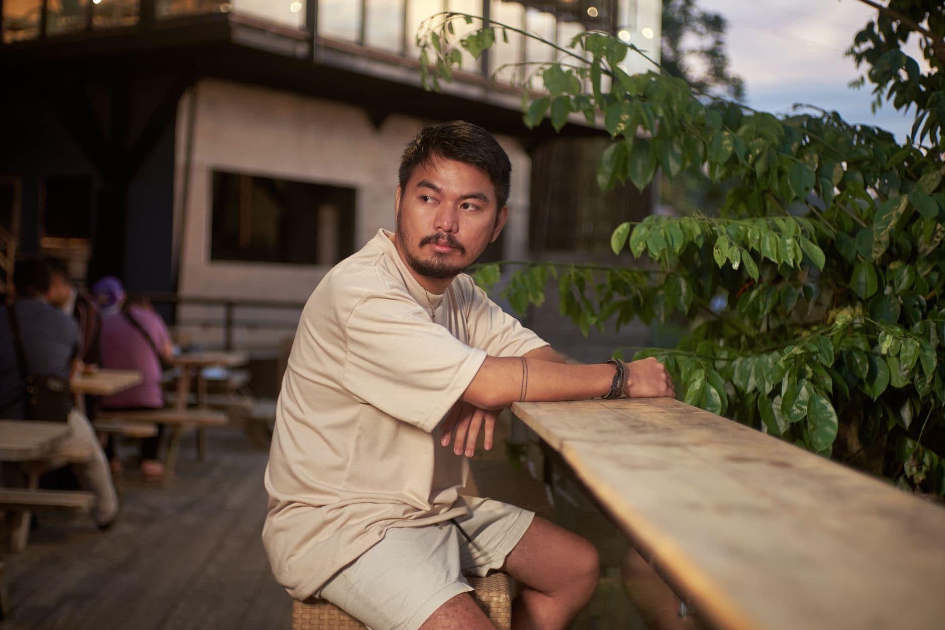 Un hombre adulto está sentado junto a una barra de madera y plantas en un café.