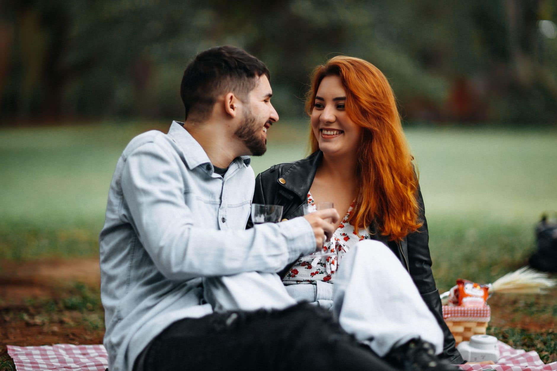 Usmiaty muž v svetlej košeli a ryšavá žena sedia s pohármi na piknikovej deke