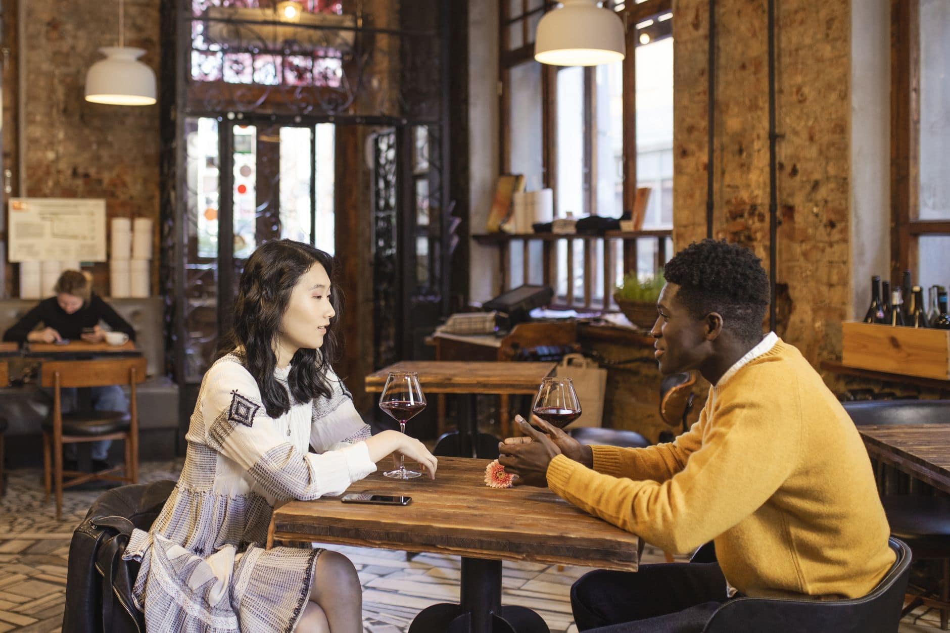 Une femme et un homme en pull jaune discutent autour de deux verres à une table.