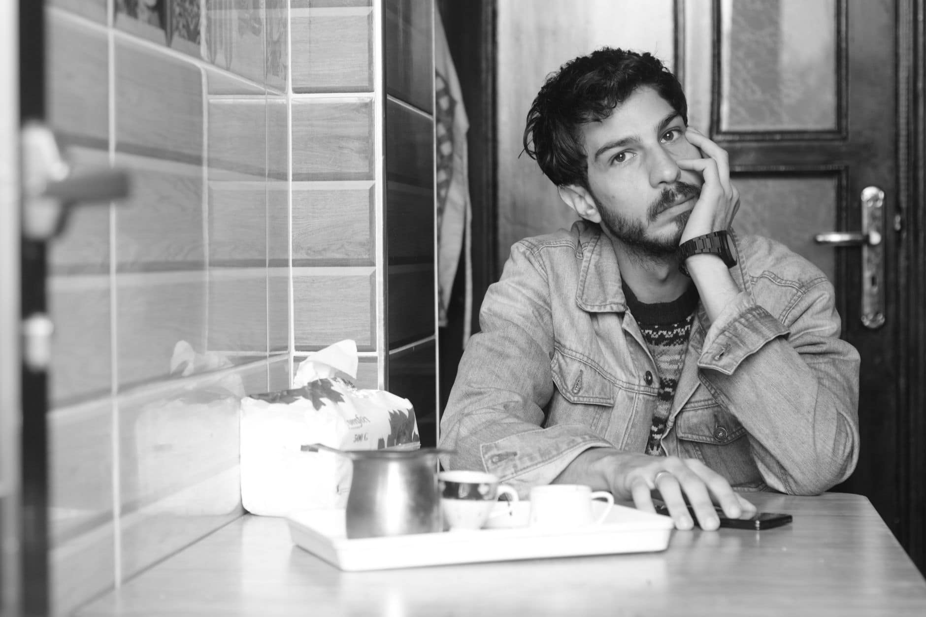 Un hombre adulto apoya la cara en una mano junto a una taza, en una foto en blanco y negro.