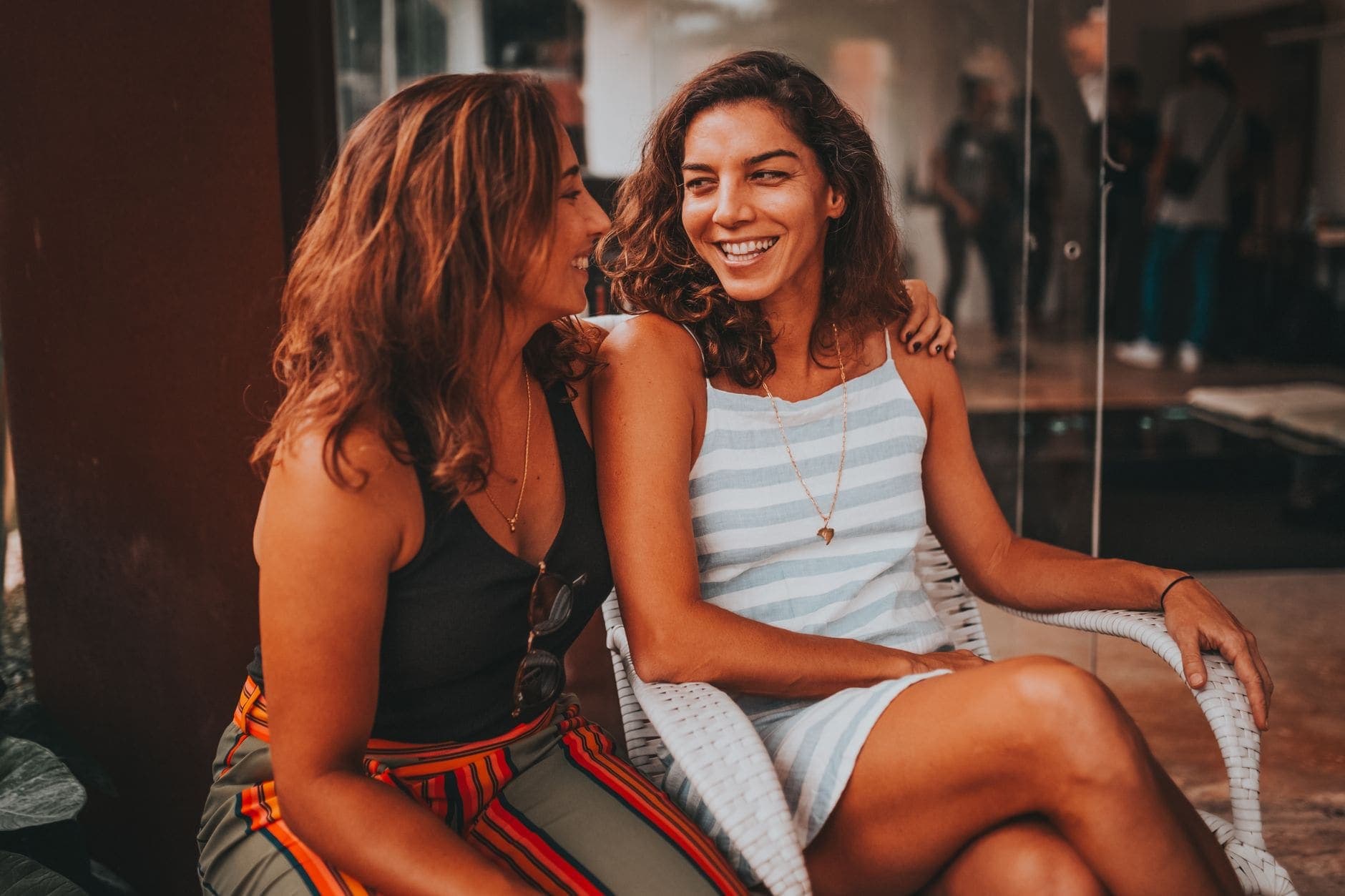 Duas mulheres sorriem lado a lado diante de uma fachada de vidro.