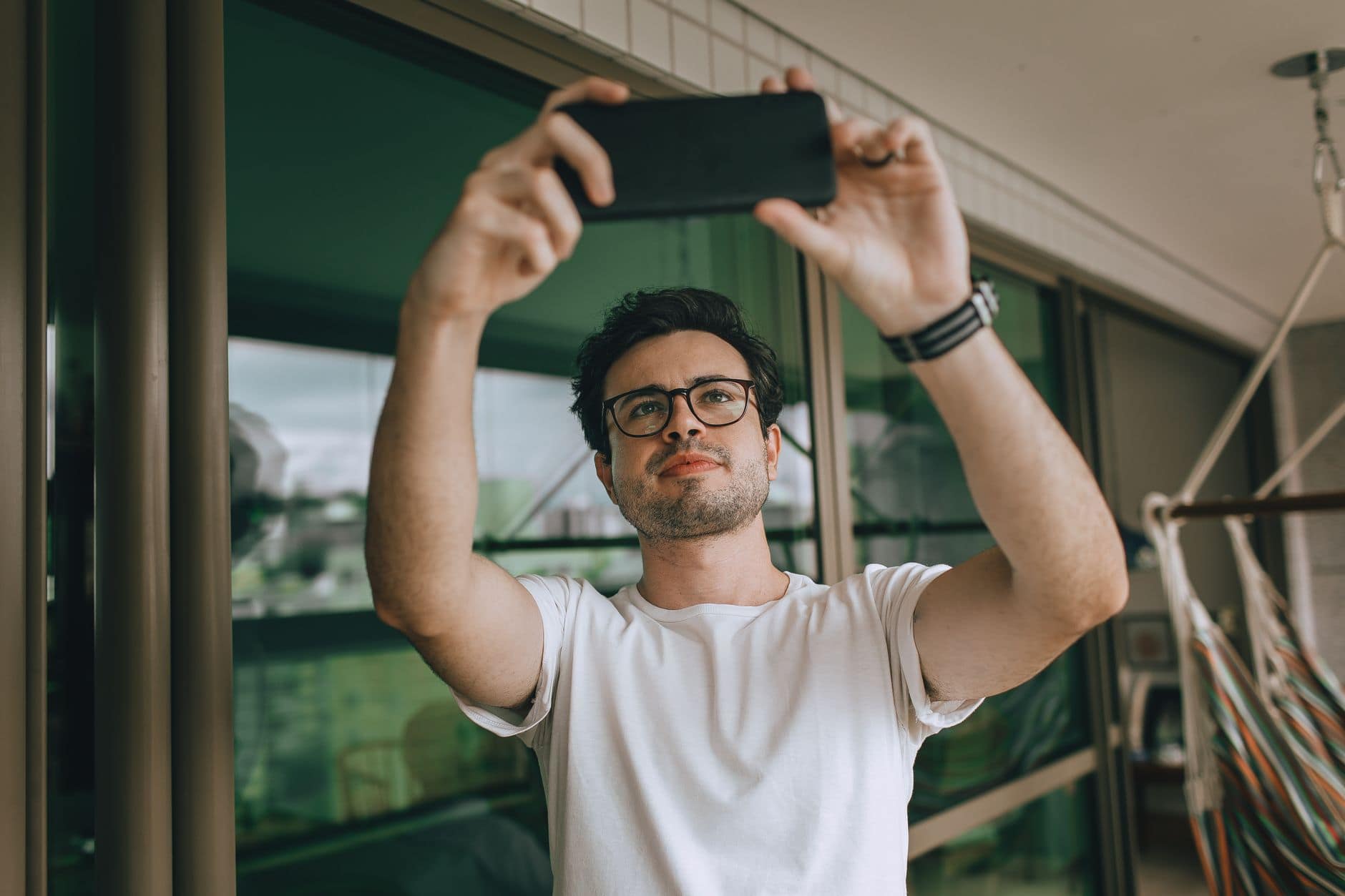Ein Mann mit Brille und weissem T-Shirt hält sein Smartphone vor sich.