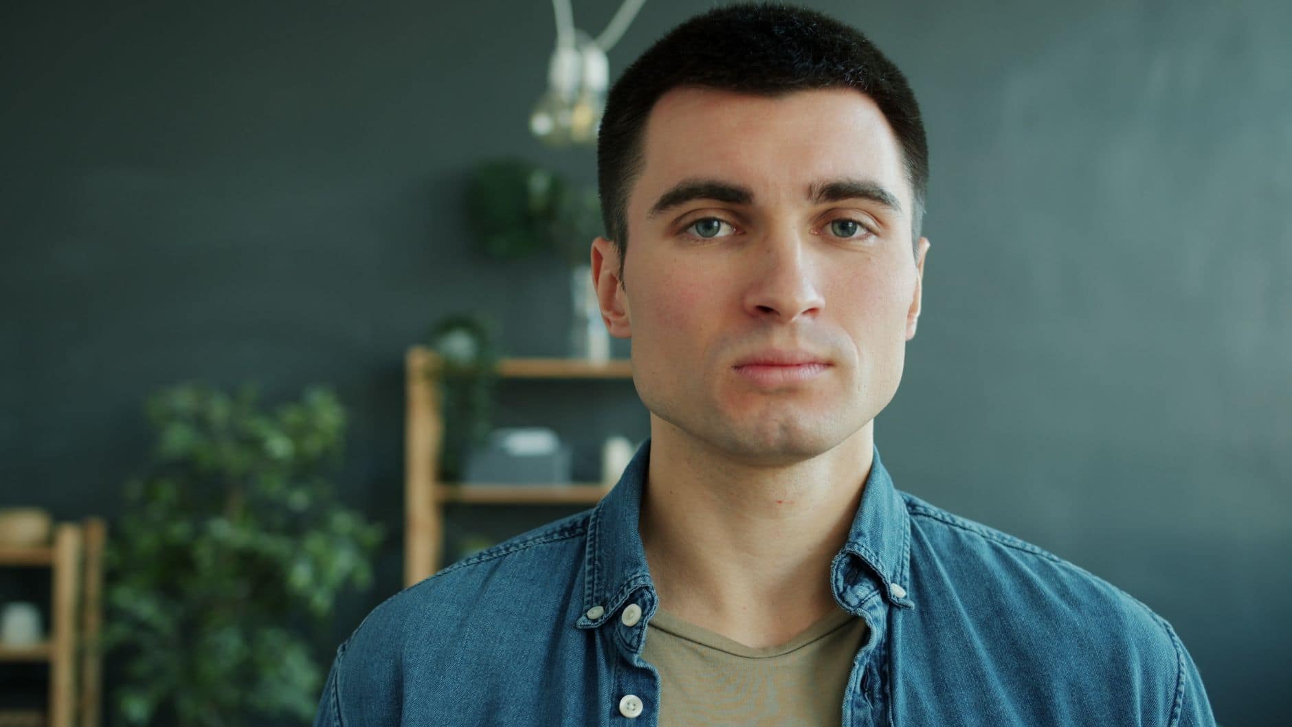 Portret kratkolasega moškega v džins srajci pred zeleno steno in rastlinami