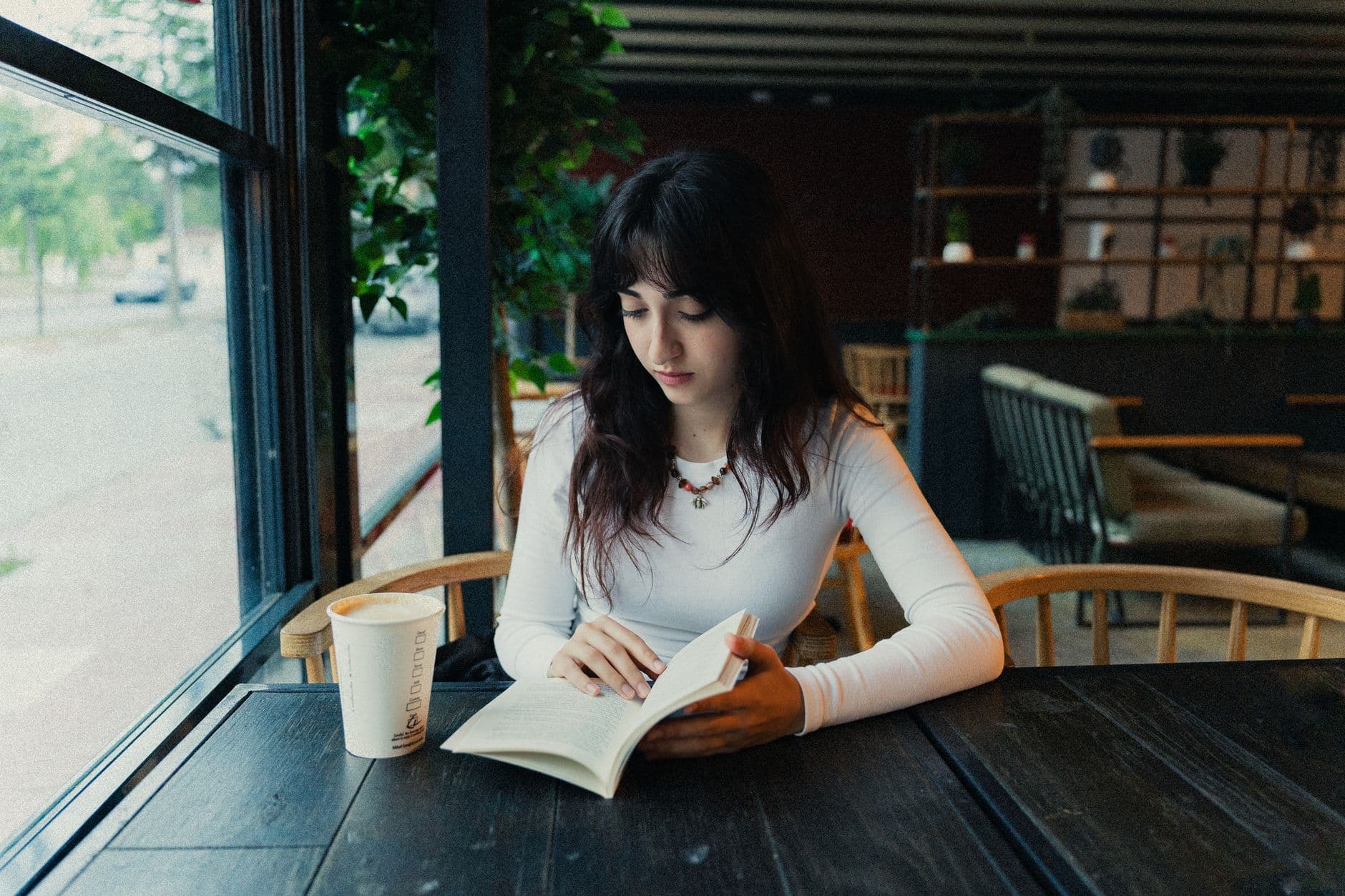 Una donna legge un libro al tavolo di un bar.