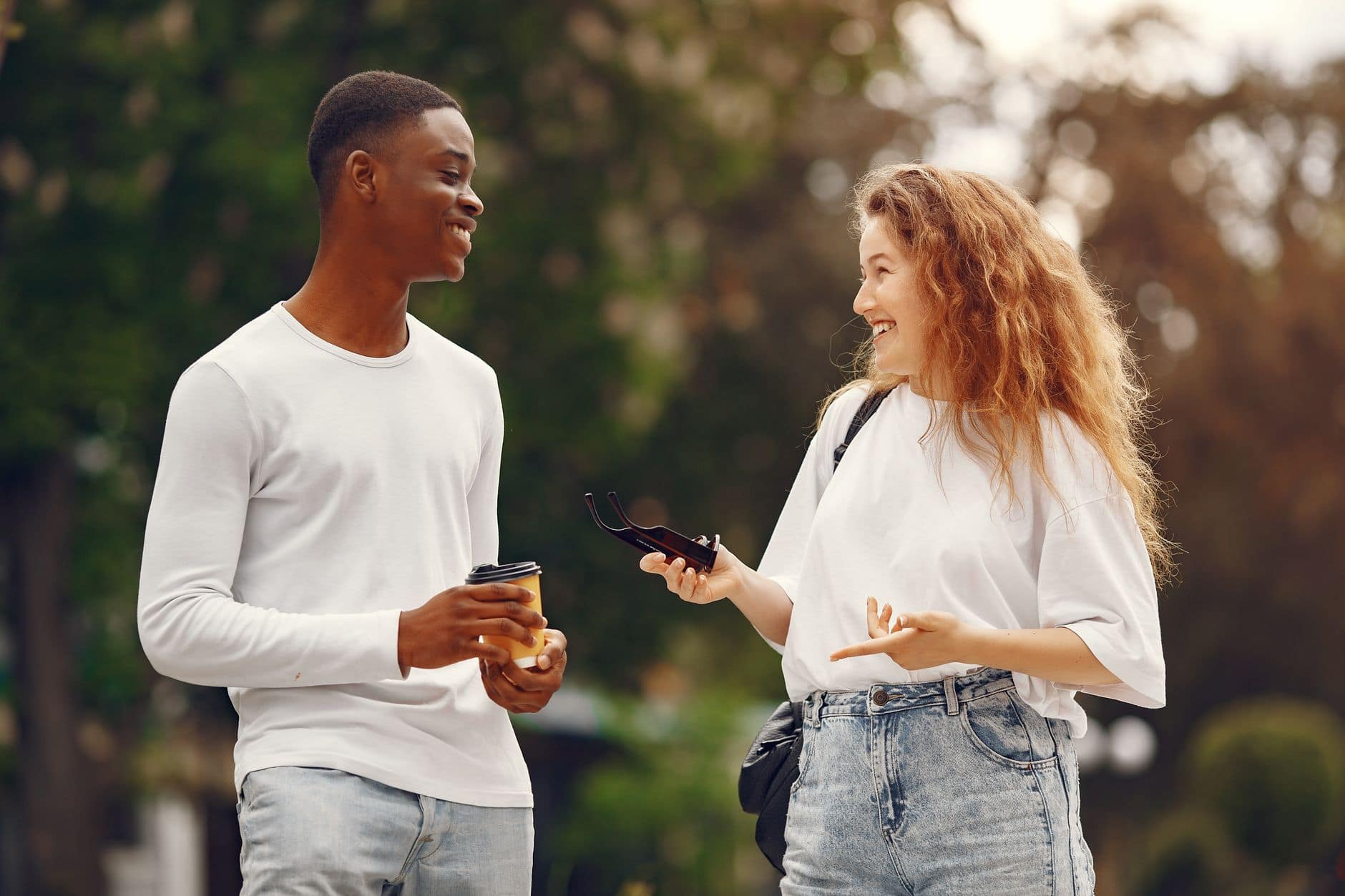 Un homme et une femme en hauts blancs se sourient en discutant dehors.