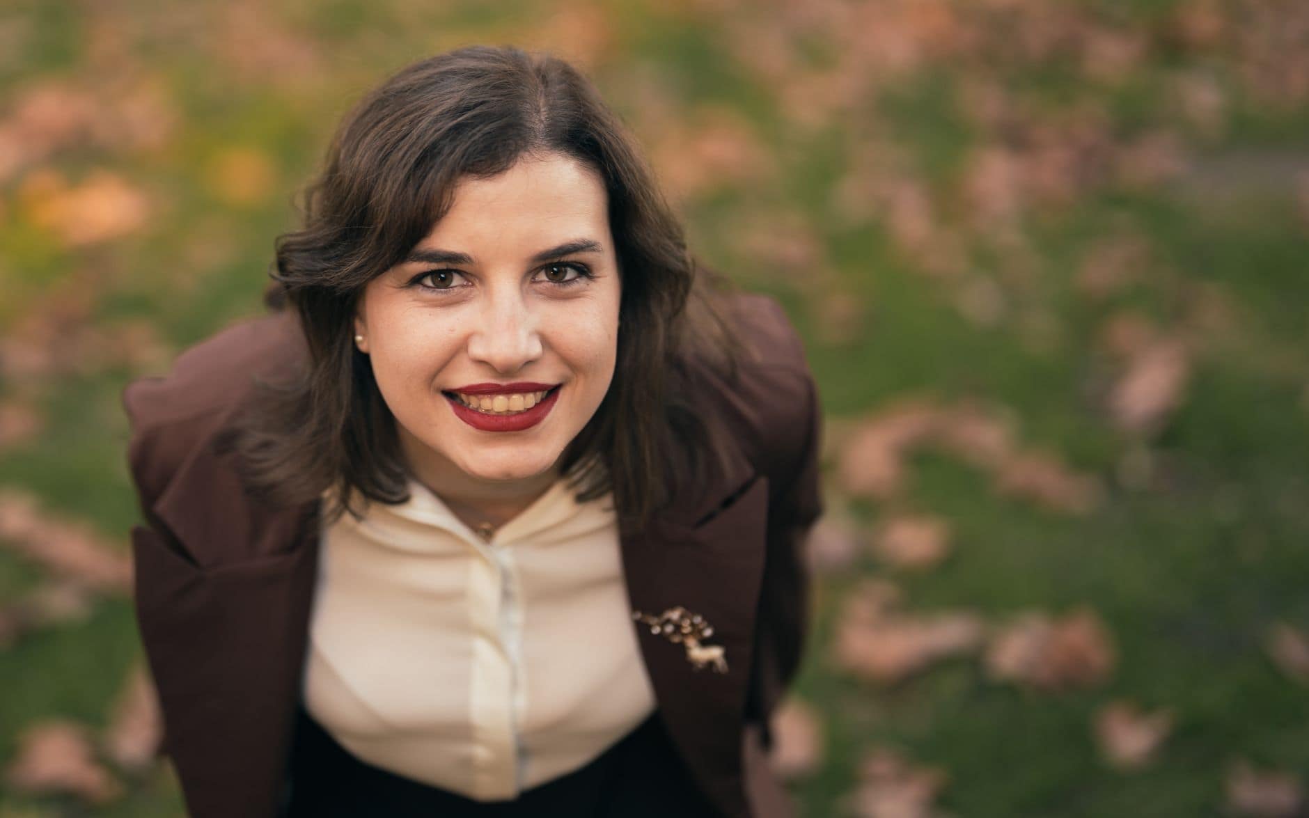 Une femme souriante en veste brune regarde l'objectif, avec de l'herbe en arrière-plan.