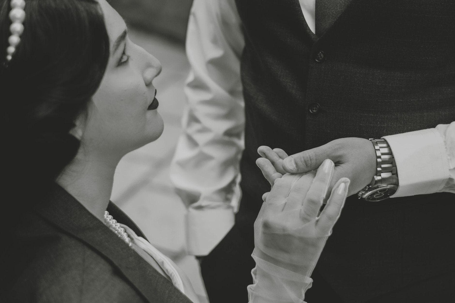 In zwart en wit: een vrouw met parels in het haar houdt de hand vast van een man in gilet met horloge