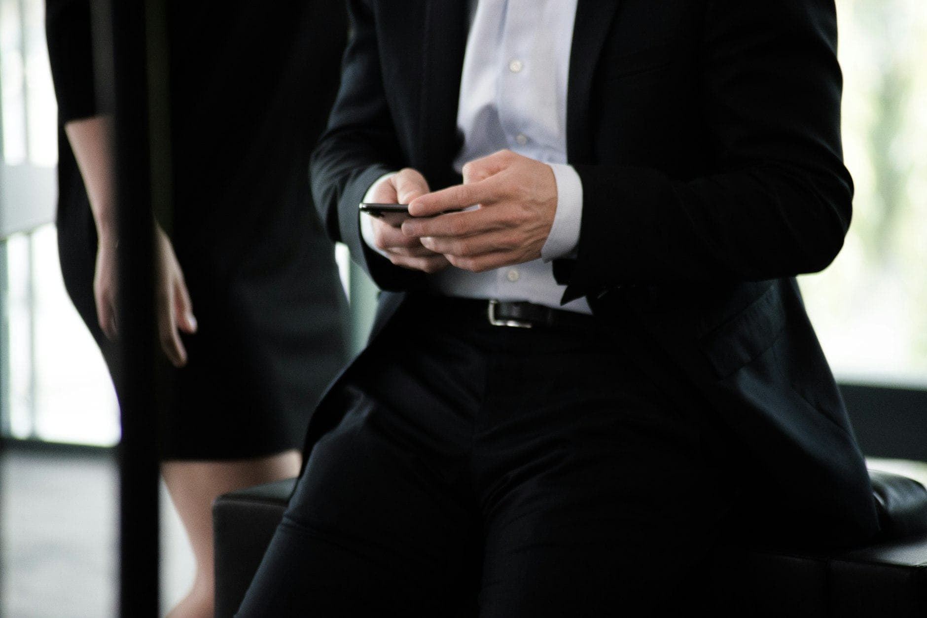 Man in a black suit and white shirt checking his phone, with his face out of frame