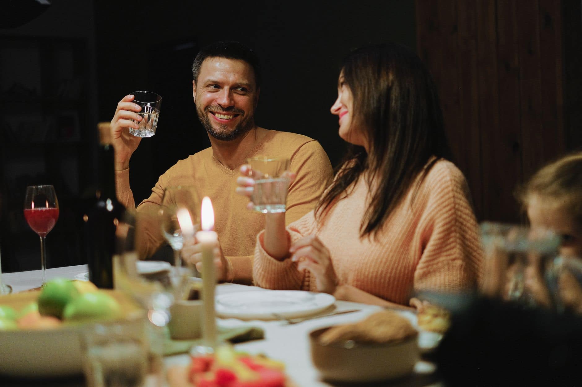 Dos personas adultas sonríen y levantan sus vasos durante una cena con velas.