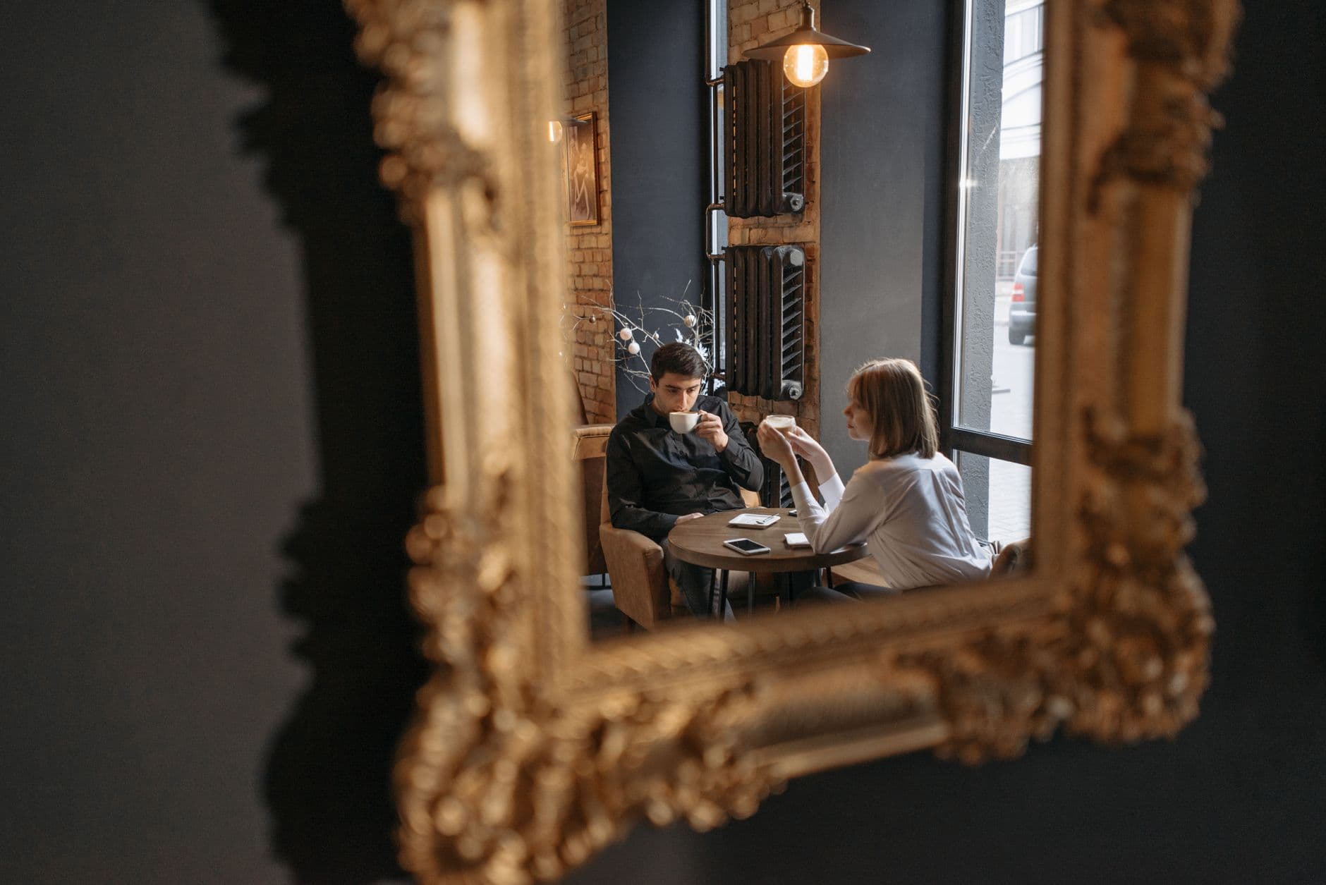 Ein Paar bei Kaffee an einem Cafétisch, gesehen im Spiegel eines goldenen Rahmens.
