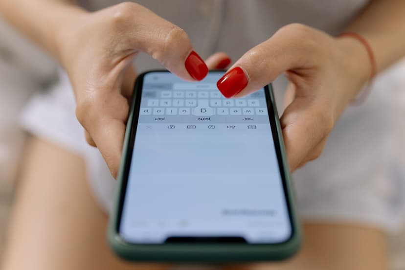 Närbild av kvinnohänder med rödmålade naglar som skriver ett meddelande på mobilens tangentbord