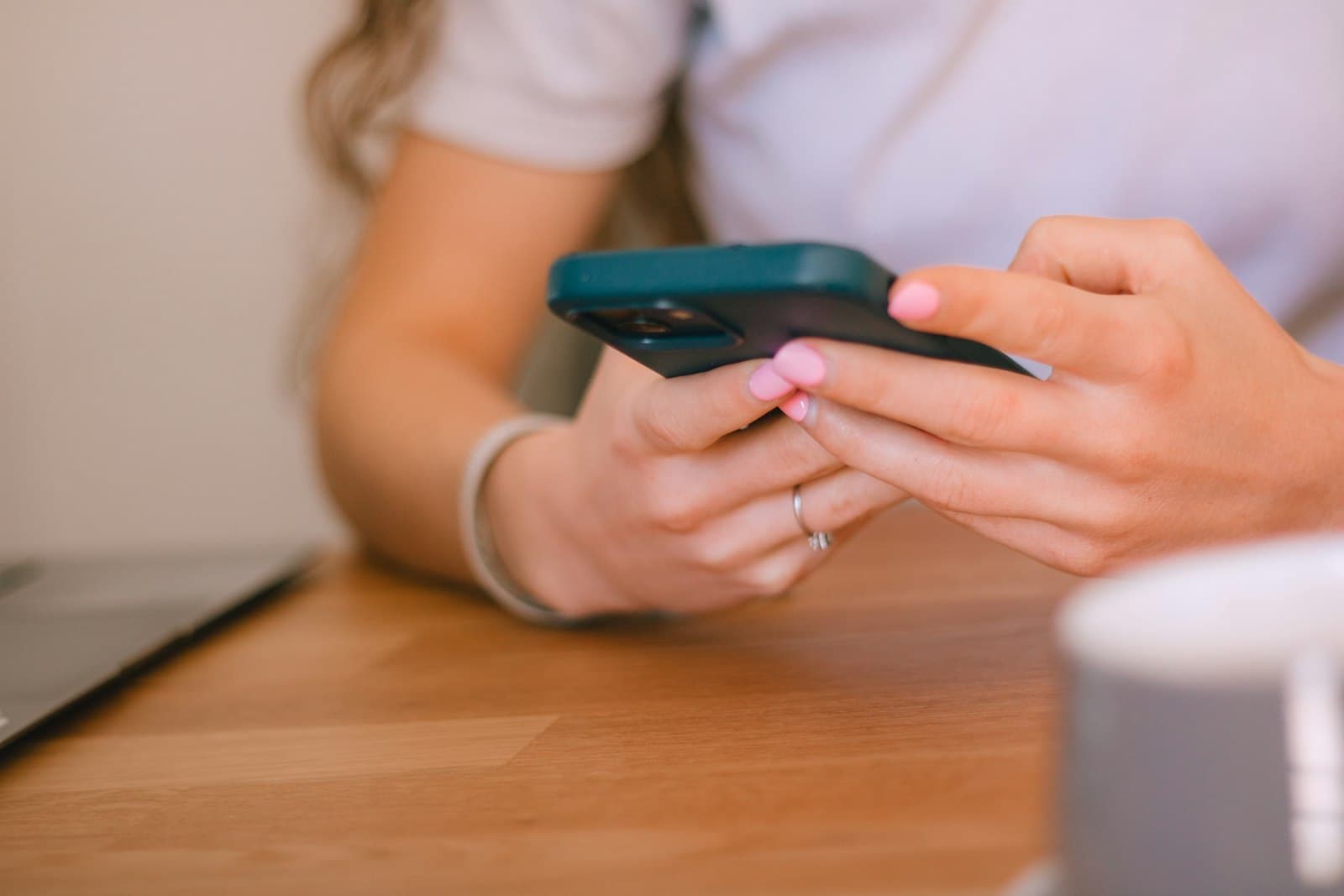 Frauenhände mit rosa Nägeln tippen an einem Holztisch auf einem Smartphone