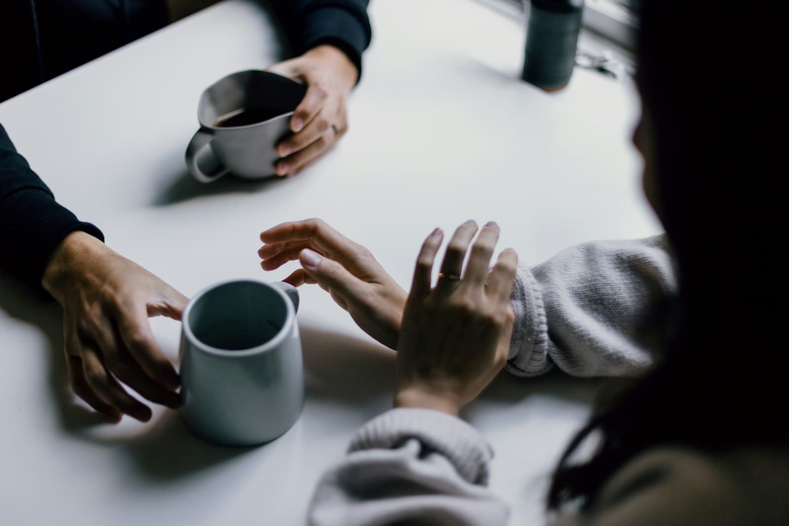 Zwei Personen im ruhigen Gespräch am Tisch, zu sehen sind nur ihre Hände und Kaffeebecher