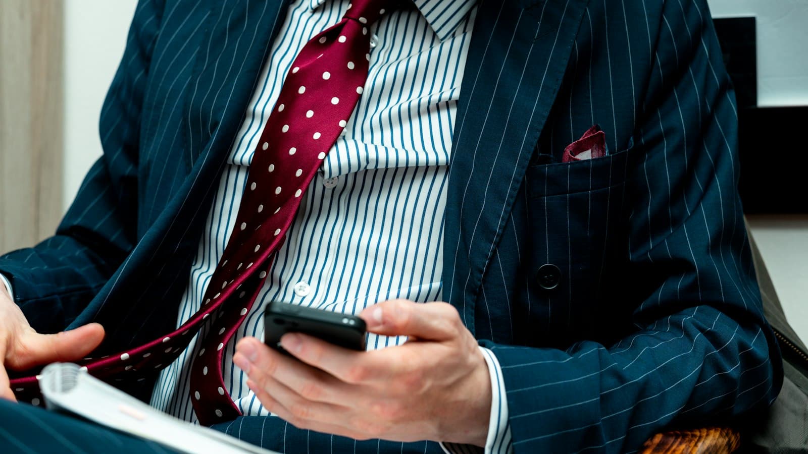 Mann im Nadelstreifenanzug mit gepunkteter Krawatte tippt auf seinem Smartphone