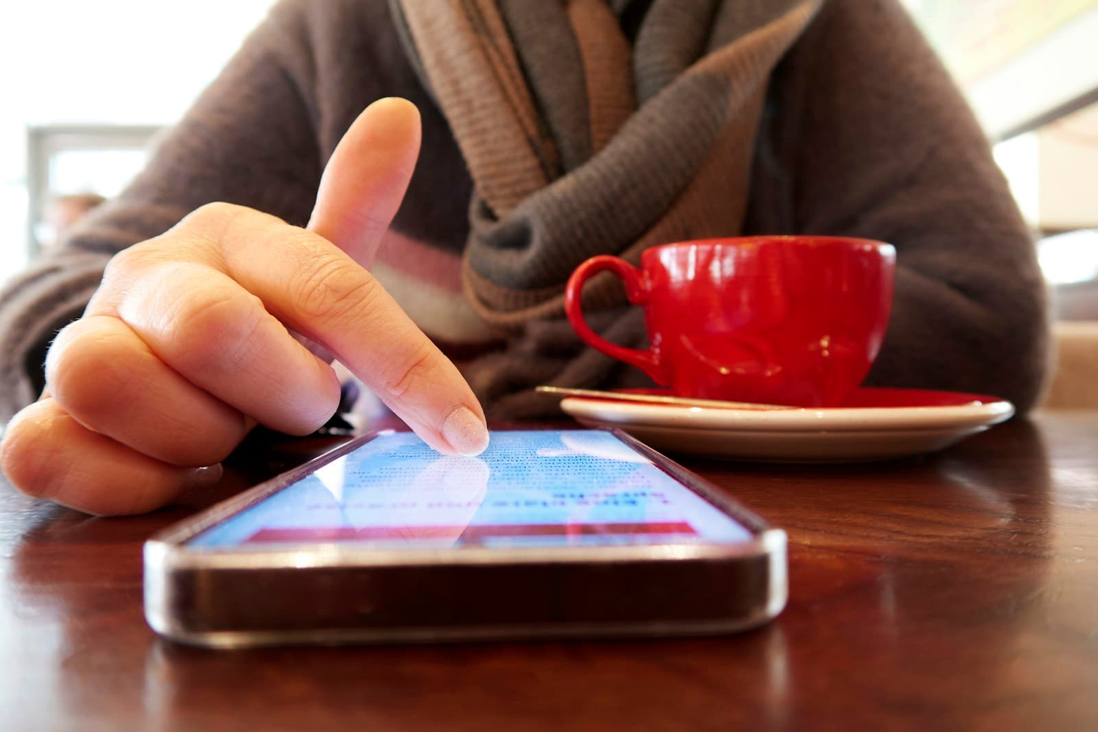 Hand tippt auf ein Smartphone auf einem Cafétisch neben einer roten Espressotasse