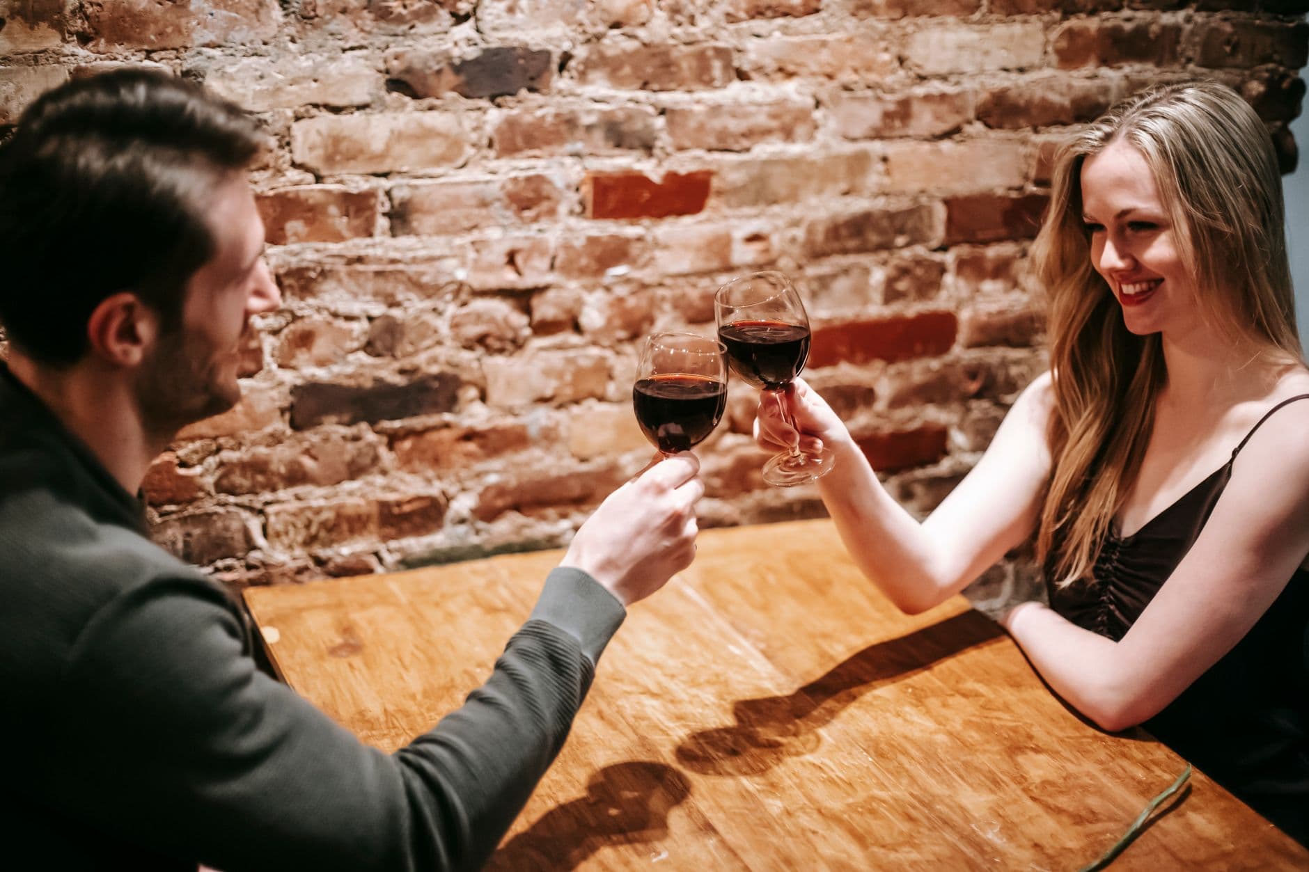 Ein Mann und eine Frau stoßen in einem Lokal mit Rotwein an und lächeln sich zu.