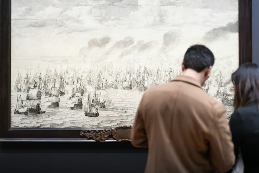 A couple seen from behind in a museum gallery, looking at a large framed drawing of sailing ships