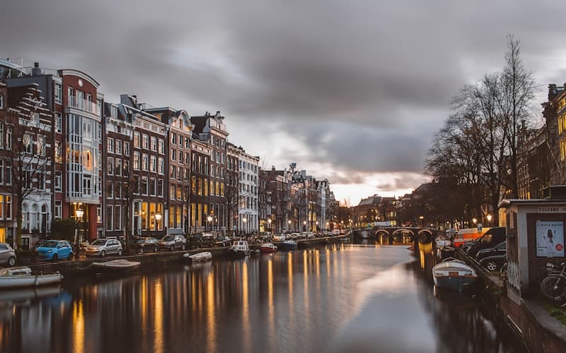 Gracht met oude grachtenpanden, afgemeerde boten en lantaarns onder een bewolkte lucht.