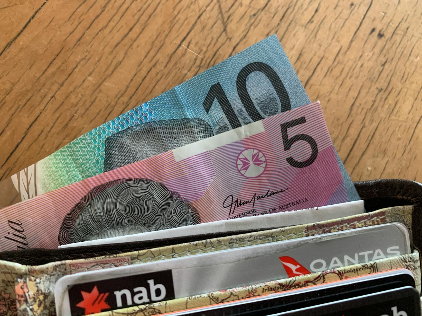 Australian ten and five dollar notes tucked into a worn wallet on a wooden table.