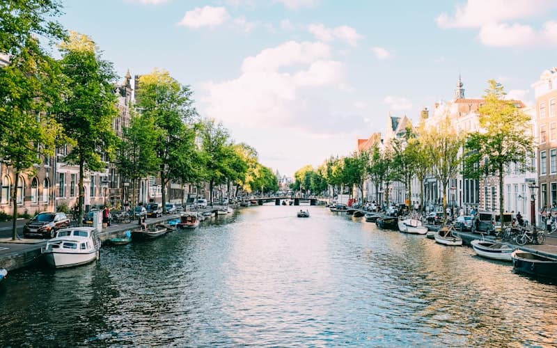 Brede gracht met bomen, aangemeerde bootjes en zonlicht op de gevels in de zomer.