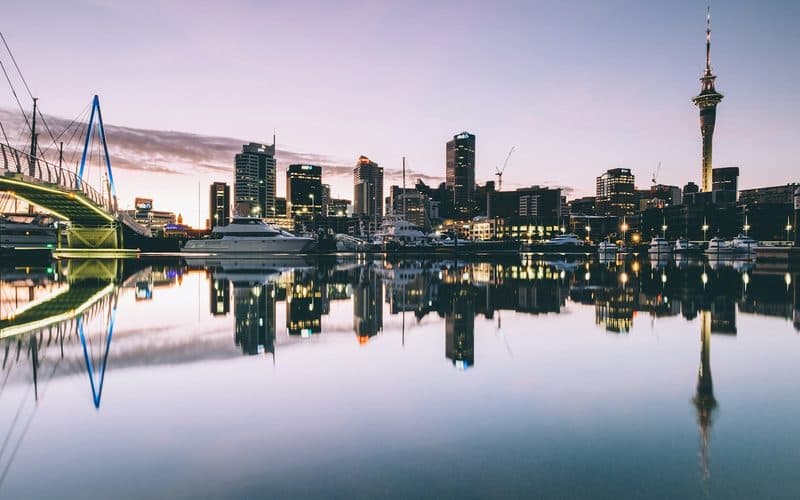 Harbour skyline and moored boats mirrored in still water at dusk under a pink sky.